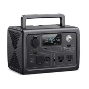 A front-angled studio product photo of the compact BLUETTI EB3A portable power station, US version, against a white background. The unit features a dark charcoal grey body, a centred LCD display showing 99% battery, two US AC outlets, and a built-in LED flashlight.